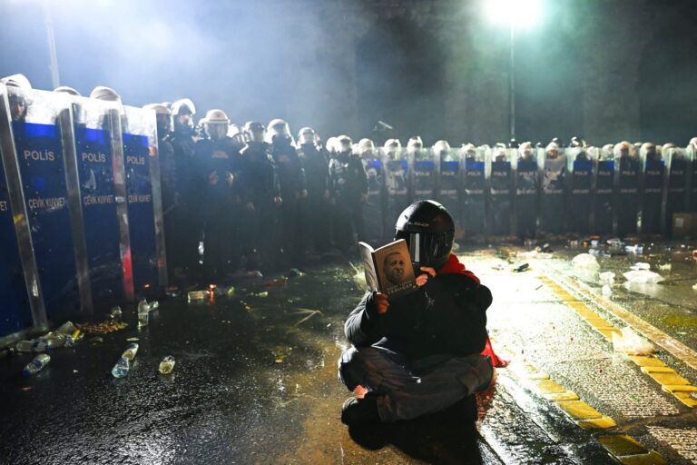 A protester sits with a book about Turkish President Recep Tayyip Erdoğan in front of Turkish anti-riot police officers during a rally in support of Istanbul’s arrested mayor in Istanbul