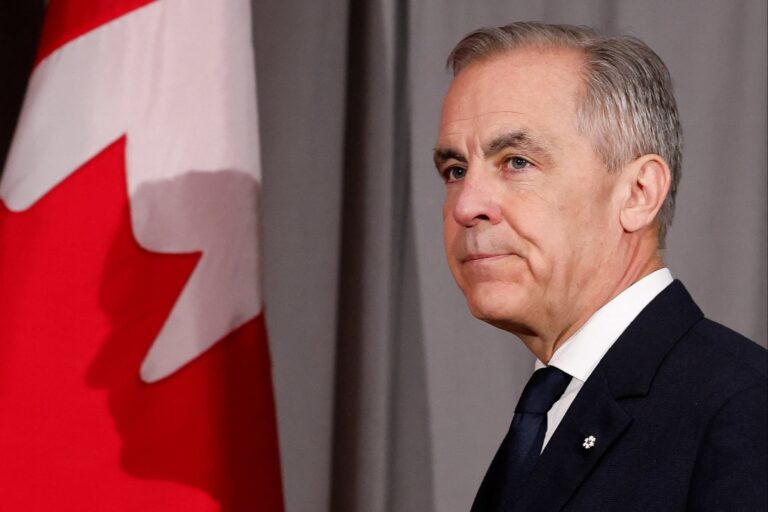 Mark Carney is seen standing in front of a Canadian flag
