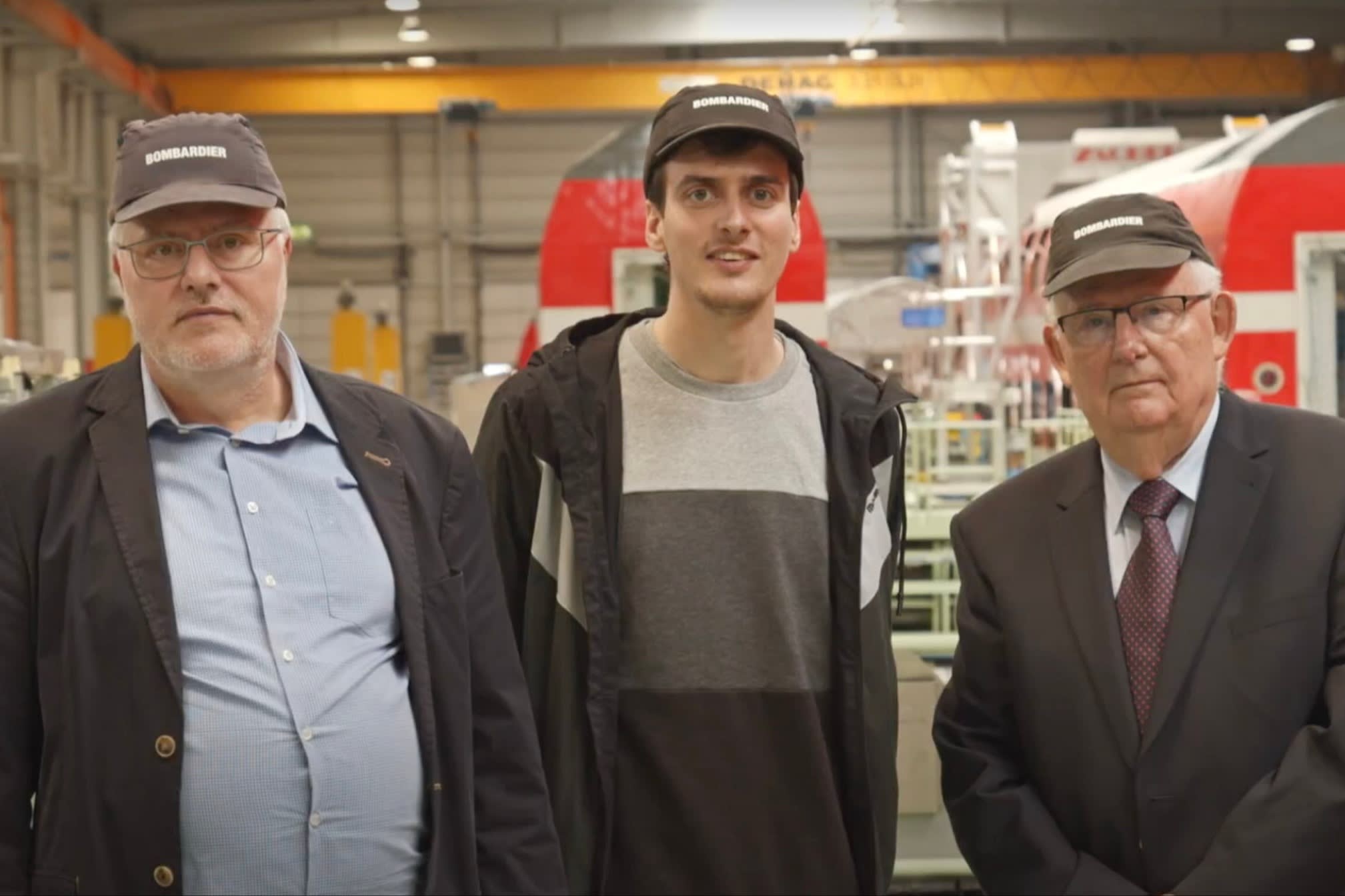 Carsten Liebig with his son and father, all wearing Bombardier caps, stand together inside the plant