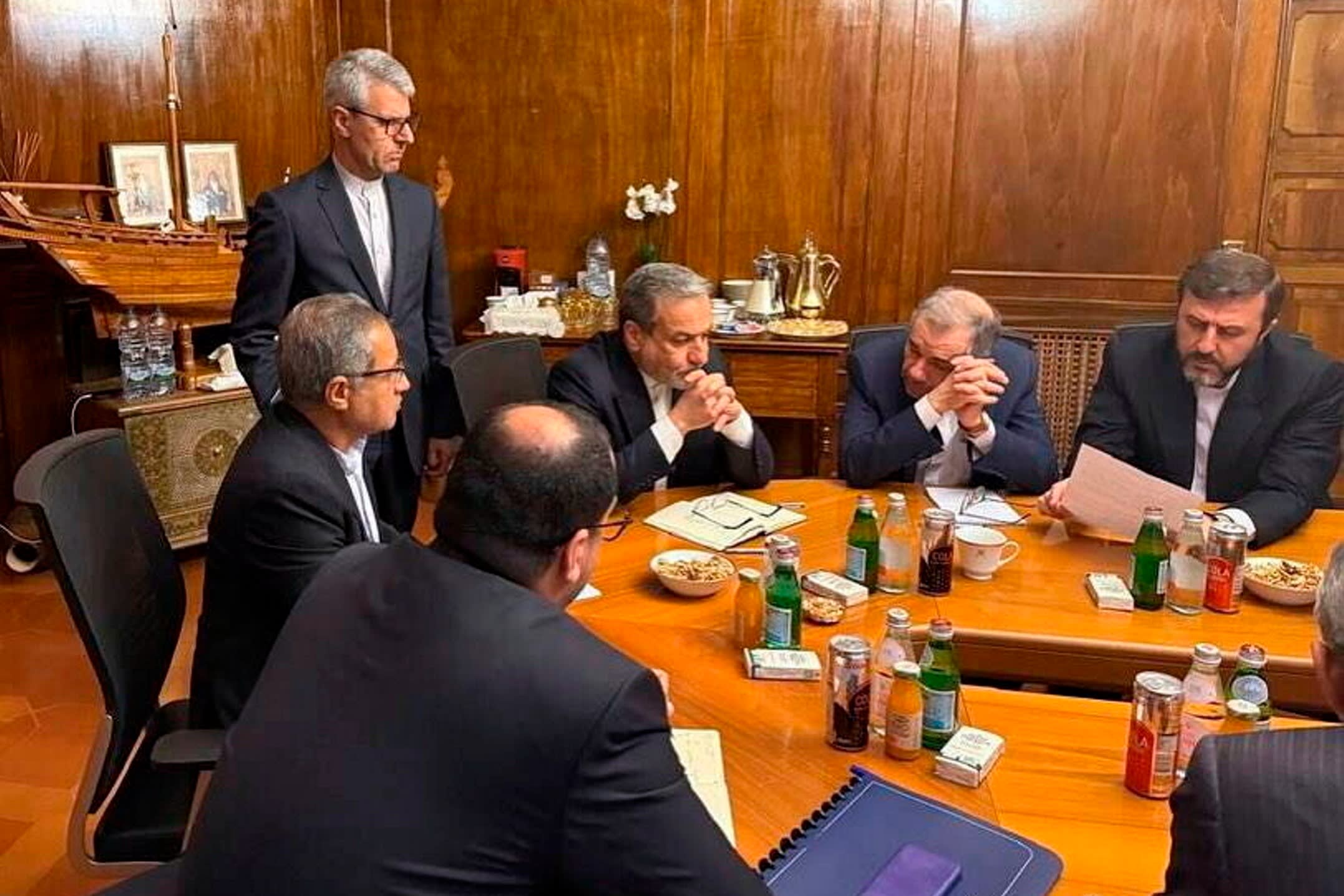 Members of the Iranian group are seated and standing around a table during their discussions