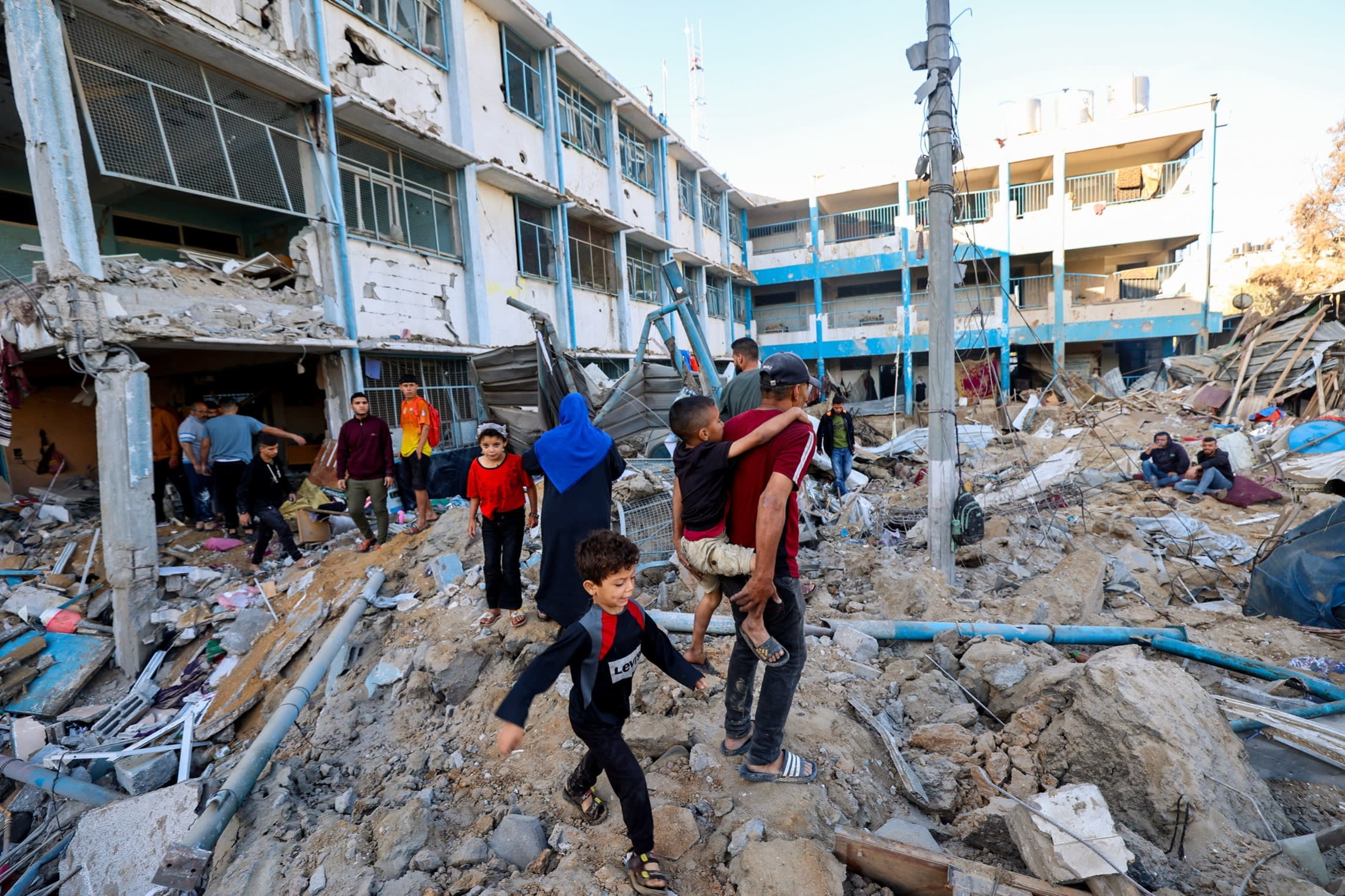 Palestinians look at the destruction at a UNRWA school housing displaced people, following an Israeli strike in the Bureij refugee camp in the centre of the Gaza Strip