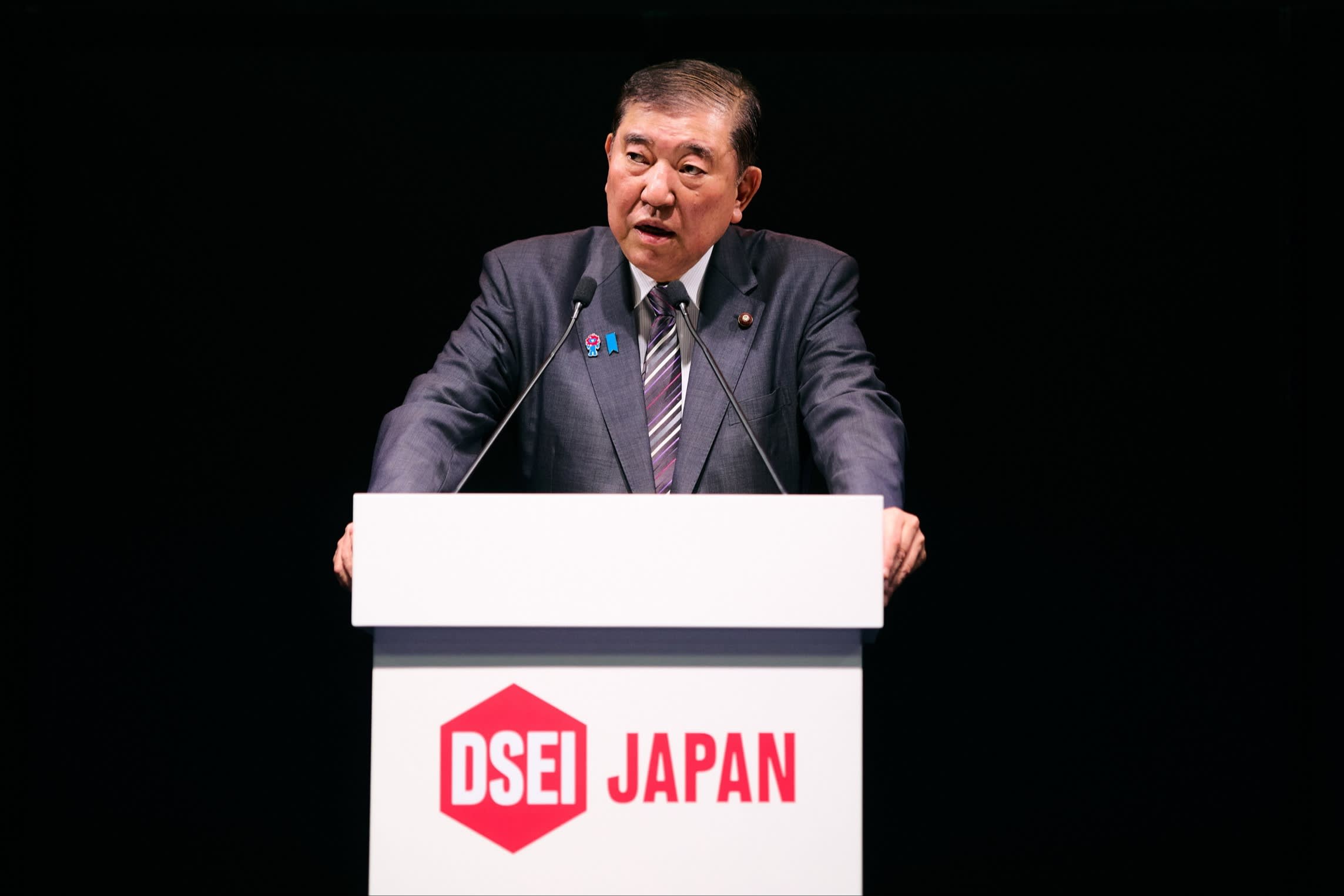 Shigeru Ishiba stands at a podium with DSEI Japan written on it, addressing an audience