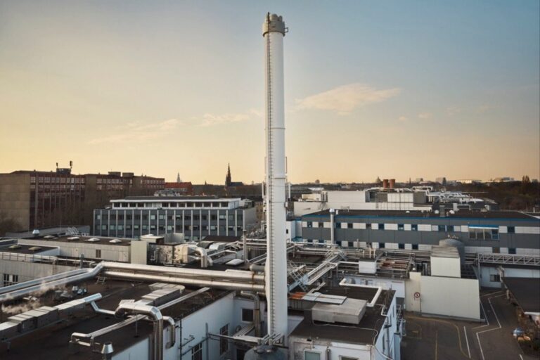 The image shows the Xellia Pharmaceuticals site, featuring a large industrial complex with interconnected buildings and numerous pipes