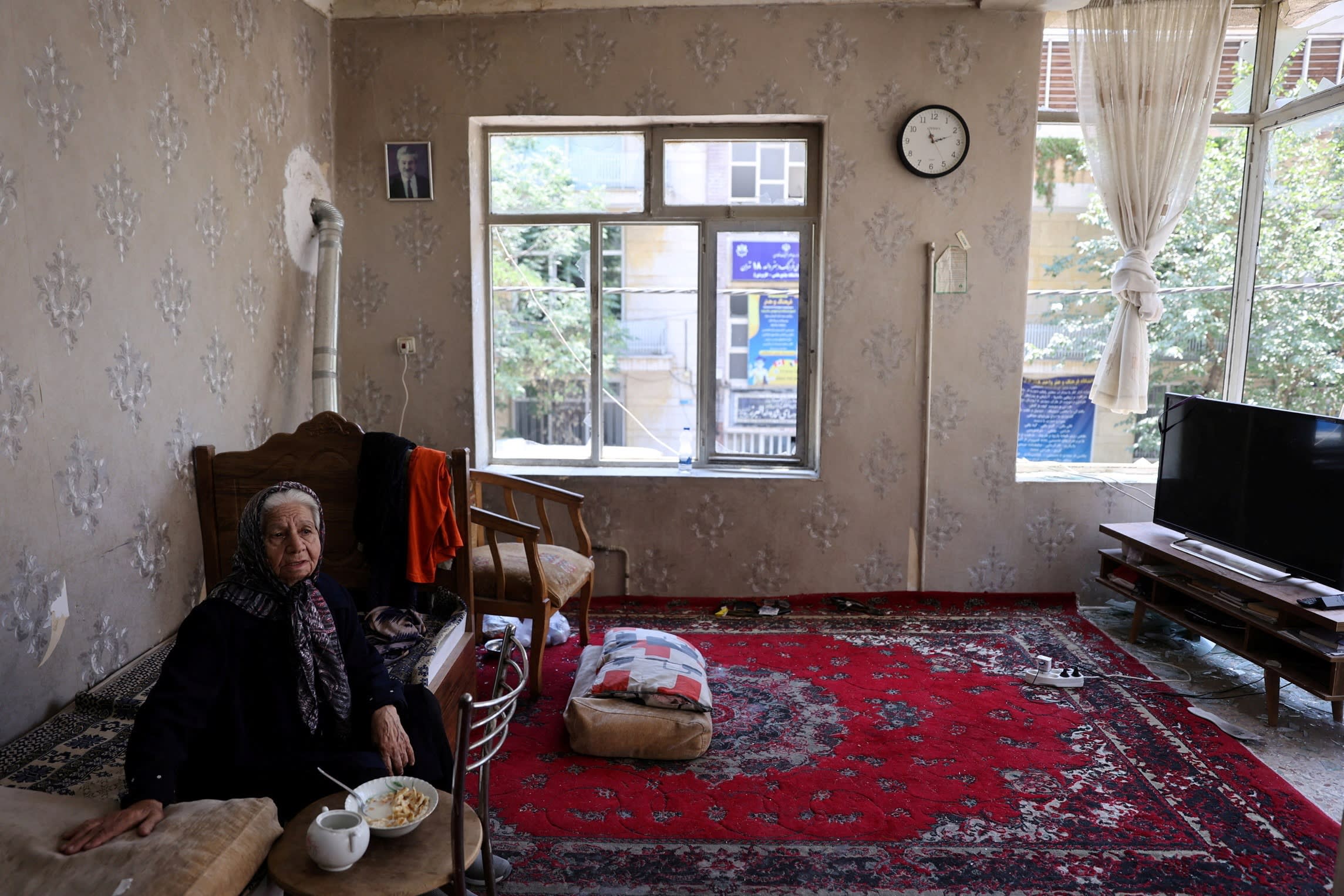 A woman sits inside her damaged house at an impact site following the Israeli strikes on Iran, in Tehran