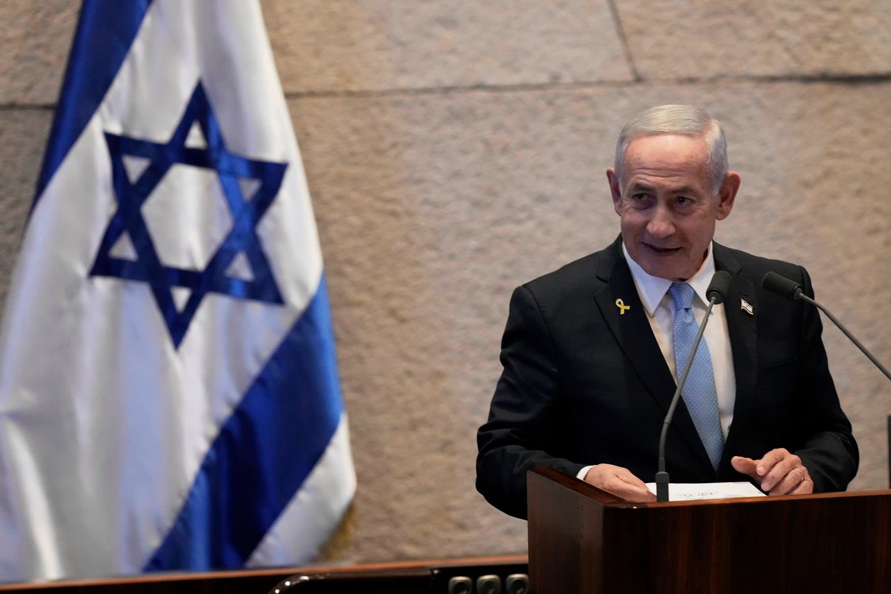 Benjamin Netanyahu stands at a podium delivering a speech, with the Israeli flag visible in the background