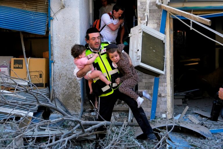 A rescue worker evacuates two children from the site where a missile launched from Iran struck in Haifa
