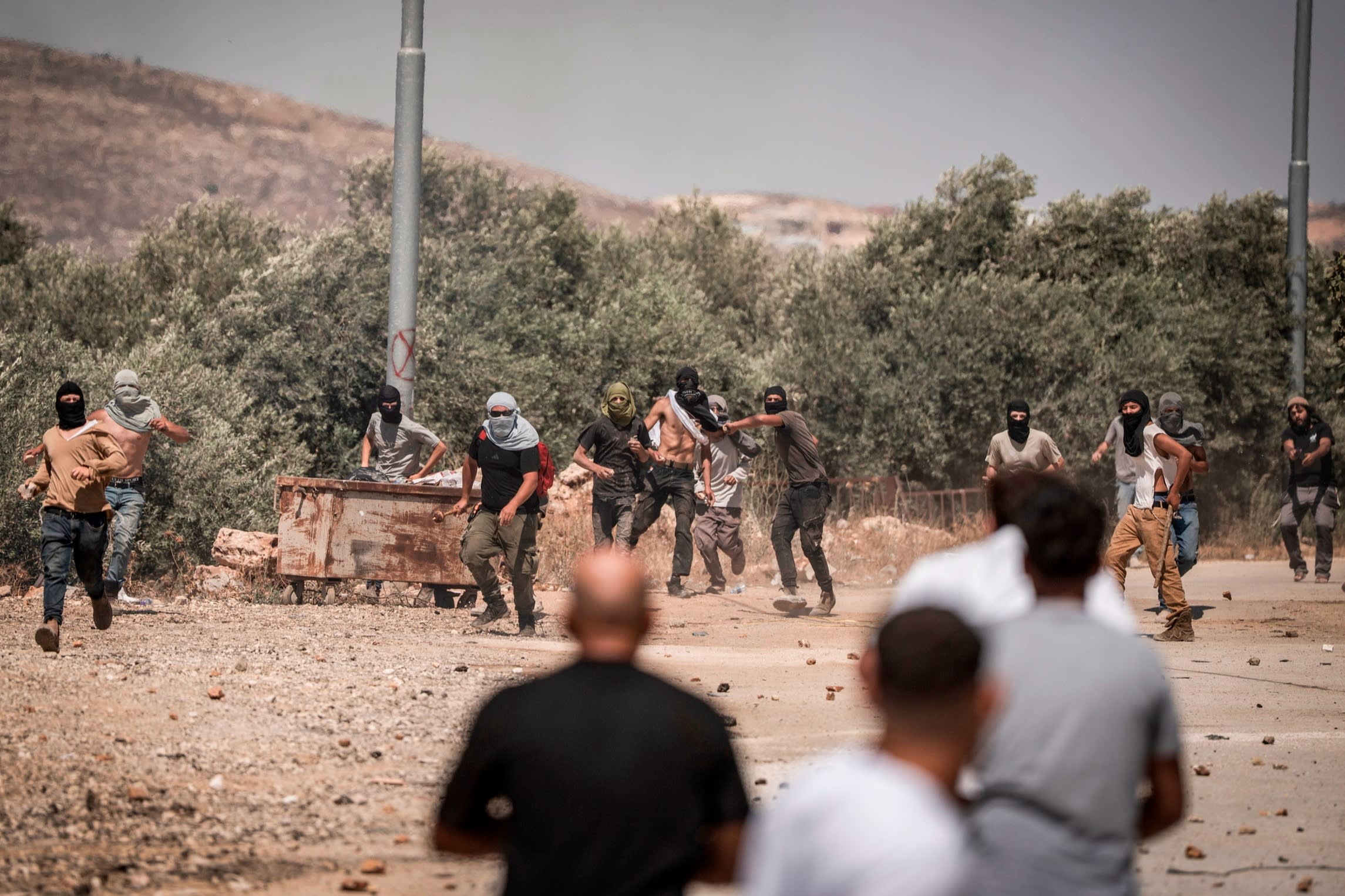 Israeli right-wing settlers throw stones towards Palestinian villagers during an attack on the West Bank village of Turmusaya