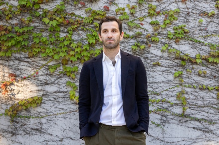 Max Ullman stands in front of a wall covered with green ivy, wearing a dark blazer and white shirt.