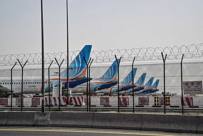 Several FlyDubai planes parked behind a barbed-wire fence at Dubai International Airport.