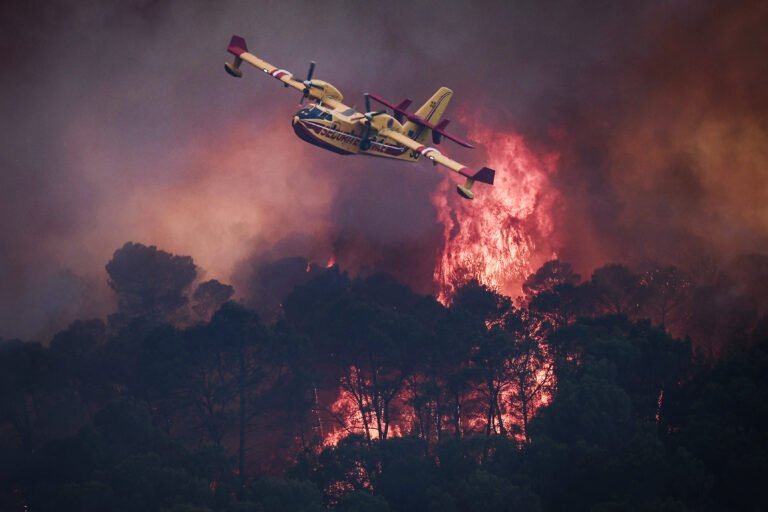 A French Civil Security Canadair CL-415 aircraft flies past flames burning a forest surrounding Cotignac, southeastern France on July 23, 2026 during a wildfire.