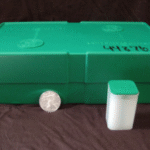 Green cardboard Silver Eagles monster box showing mint markings with individual storage tube and one-ounce coin displayed for size comparison.