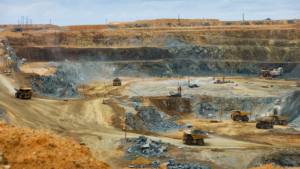 South African open-pit mine with heavy haul trucks and drilling rigs extracting ore from terraced rock walls